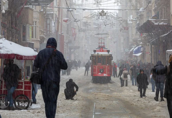 雪の下でイスタリックストリートを歩く人々と同時に その途中で歴史的な赤いトラム — ストック写真