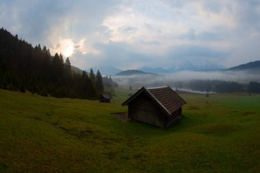 Orman kenarında dağ çayırında küçük bir kulübe, Geroldsee arka planda Karwendel Dağları gündoğumunda, Kaltenbrunn, Yukarı Bavyera, Almanya