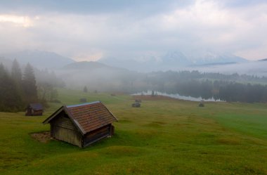 Orman kenarında dağ çayırında küçük bir kulübe, Geroldsee arka planda Karwendel Dağları gündoğumunda, Kaltenbrunn, Yukarı Bavyera, Almanya