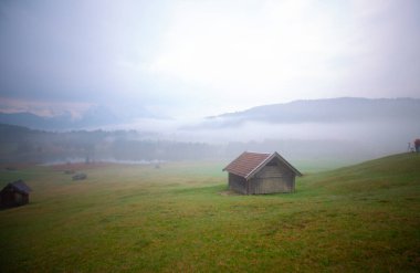Orman kenarında dağ çayırında küçük bir kulübe, Geroldsee arka planda Karwendel Dağları gündoğumunda, Kaltenbrunn, Yukarı Bavyera, Almanya