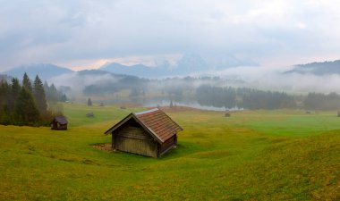 Orman kenarında dağ çayırında küçük bir kulübe, Geroldsee arka planda Karwendel Dağları gündoğumunda, Kaltenbrunn, Yukarı Bavyera, Almanya