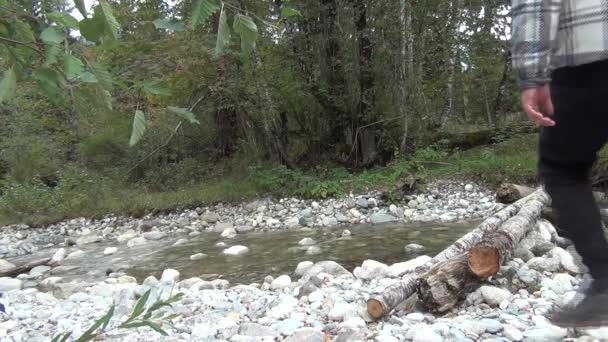 Ένας άντρας με καρό σακάκι διασχίζει το ποτάμι και ισορροπεί σε ένα κούτσουρο. — Αρχείο Βίντεο