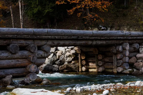 Temiz bir dağ nehrinin üzerinde büyük kütüklerden yapılmış bir köprü. Kafkasya dağlarında sonbahar. DamkHurts Nehri