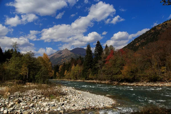 Bir dağ zirvesi, berrak bir dağ nehri ve güzel güneşli bir günde mavi gökyüzünde beyaz bulutlar. Laba Nehri, Zakan Tepesi. Ekim