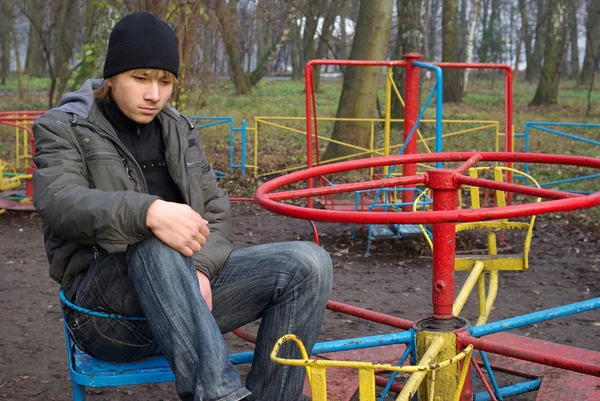 Rapaz triste num antigo parque infantil abandonado — Fotografia de Stock