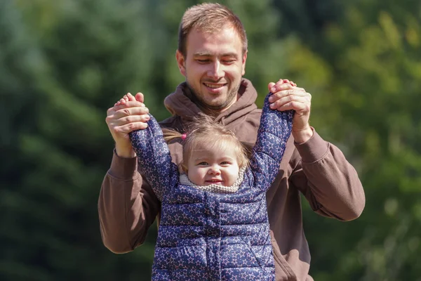 Father lifting a cheerful toddler daughter outdoors in nature