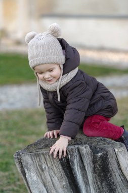 Girl playing on old tree stump in a public park