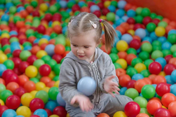 A little blond girl play in a ball pool full of multi colored ball