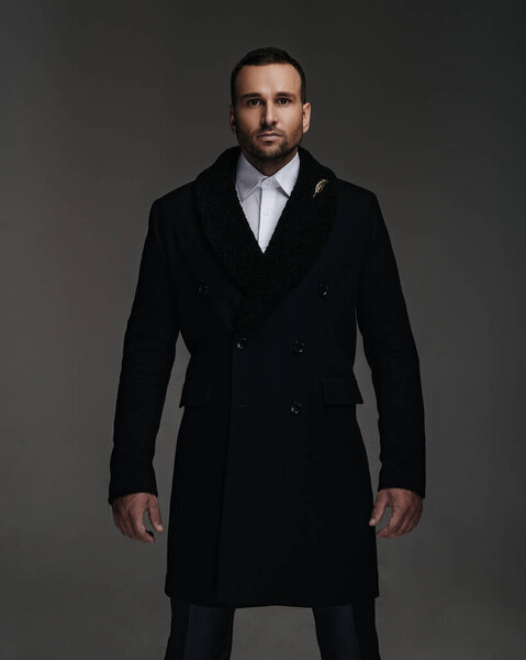 Красивый мужчина в черном зимнем пальто стоит в студии