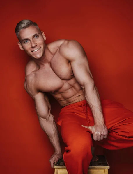 happy young guy in red sportswear laughs on red background. Smiling muscular man with six pack abs. handsome sports guy with a snow-white smile in red sweatpants.