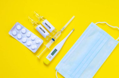 Ampul, maske, şırınga, termometre ve aşı ampulleri sarı arka planda. Yüksek kalite fotoğraf