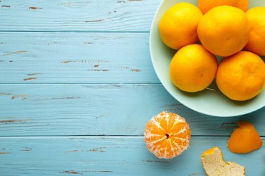 Mavi ahşap arka planda naneli kase üzerinde taze mandalina meyvesi. Üst görünüm.