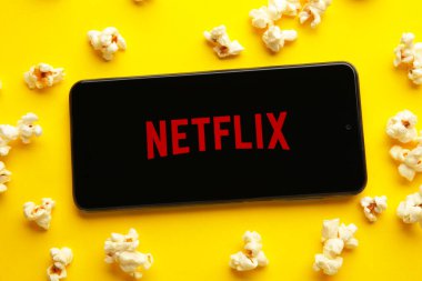 Netflix logolu akıllı telefon ve sarı arka planda patlamış mısır. Netflix, çevrimiçi medya ve videoları ve DVD 'leri posta yoluyla yayınlama konusunda uzmanlaşmıştır. Üst görünüm