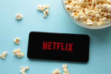 Netflix logolu akıllı telefon ve mavi arka planda patlamış mısır. Netflix, çevrimiçi medya ve videoları ve DVD 'leri posta yoluyla yayınlama konusunda uzmanlaşmıştır. Üst görünüm