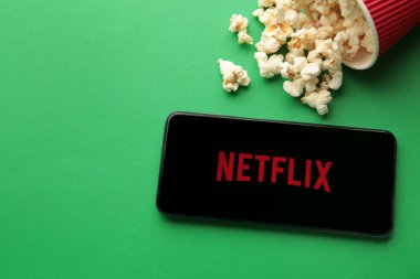 Netflix logolu akıllı telefon ve yeşil arka planda patlamış mısır. Netflix, çevrimiçi medya ve videoları ve DVD 'leri posta yoluyla yayınlama konusunda uzmanlaşmıştır. Üst görünüm