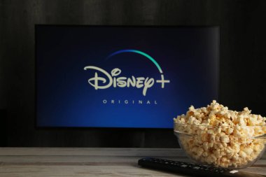 Nikolaev, Ukrayna - 20 Kasım 2021. Adamın biri patlamış mısır televizyonunda yeni ekranı olan bir Disney kumandası tutuyor. Disney bir çevrimiçi video yayınlama abonelik hizmetidir. Üst görünüm