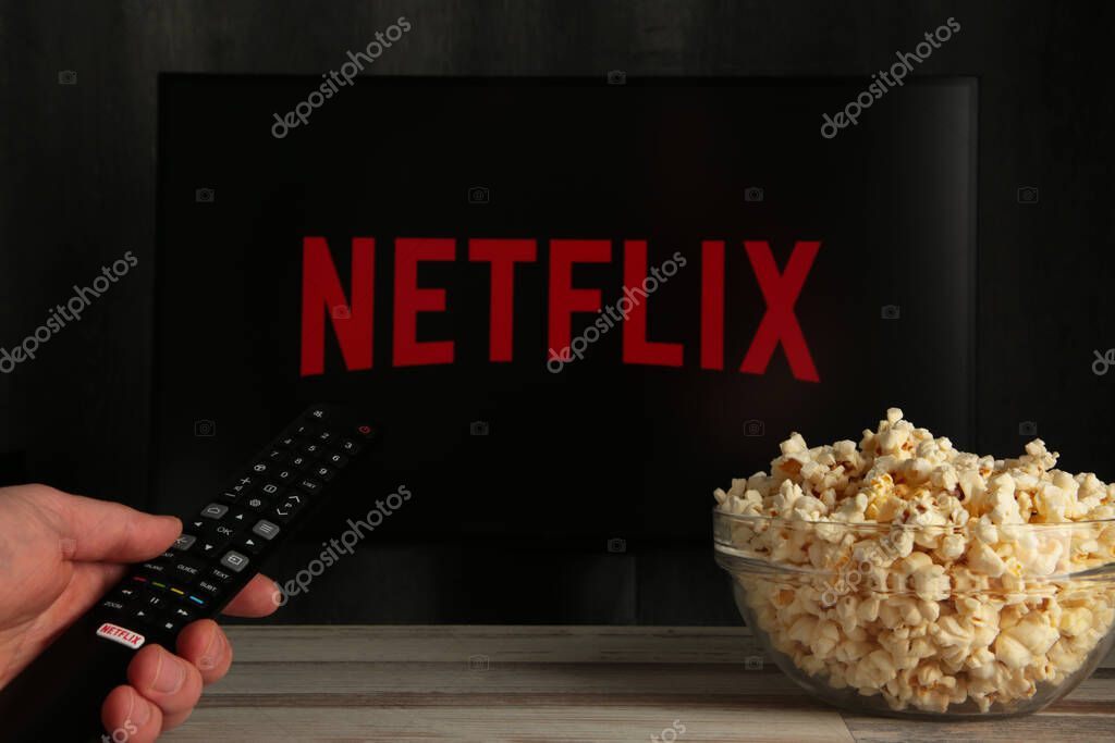 Nikolaev, Ukraine - November 20, 2021. Man with TV remote control in hand and Netflix logo in background. Netflix is the global provider of streaming movies and TV series.
