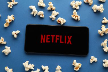 Netflix logolu akıllı telefon ve mavi arka planda patlamış mısır. Netflix, çevrimiçi medya ve videoları ve DVD 'leri posta yoluyla yayınlama konusunda uzmanlaşmıştır. Üst görünüm