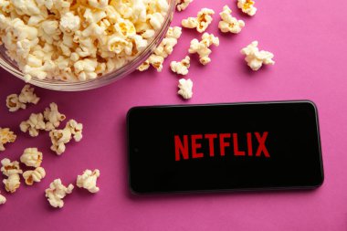 Netflix logolu akıllı telefon ve mor arka planda patlamış mısır. Netflix, çevrimiçi medya ve videoları ve DVD 'leri posta yoluyla yayınlama konusunda uzmanlaşmıştır. Üst görünüm