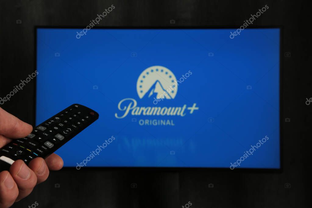 Nikolaev, Ukraine - November 20, 2021. Man with TV remote control in hand and Paramount Pictures Corporation logo in background. Top view.