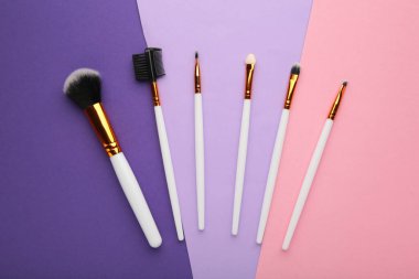 Mor ve pembe arkaplanlı çeşitli makyaj fırçaları. Üst görünüm
