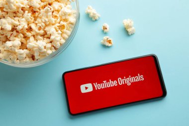 Nikolaev, Ukrayna - 20 Kasım 2021: Mavi arka planda akıllı telefondan patlamış mısır ve Youtube logosu. Üst görünüm