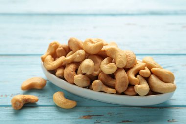 Mavi ahşap arka planda beyaz tabakta kaju fıstığı..