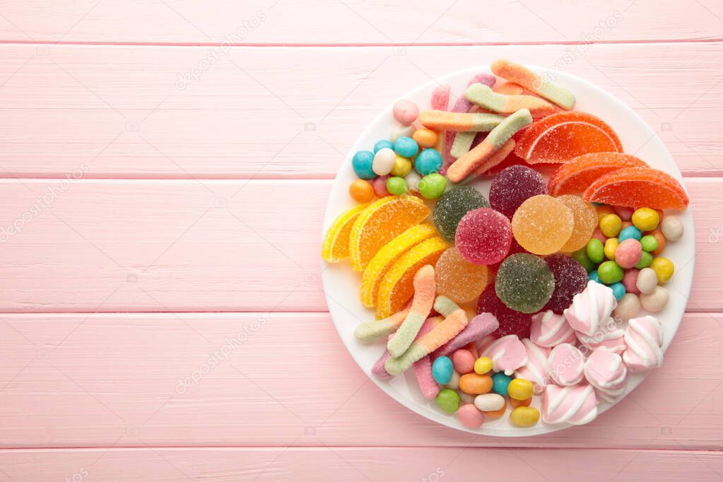 Colorful candies lollipops and jelly in plate on pink wooden background. Sweets with copy space