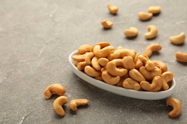 Cashew nuts on white plate on grey background.