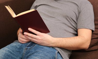 Kahverengi kanepede yatan ve evde kitap okuyan bir adam. Üst görünüm