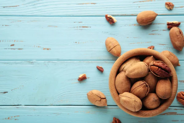 Pecan nuts on wooden bowl on blue background. Top view.