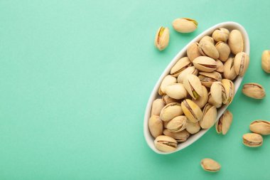 Fotokopi alanı olan yeşil arka planda beyaz plakalı Pistachios yığını. Üst görünüm.