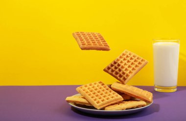 Renkli arka planda havada uçuşan Belçika waffleları. Süt ve ballı waffle tabağı. Yaratıcı gıda konsepti. Üst görünüm