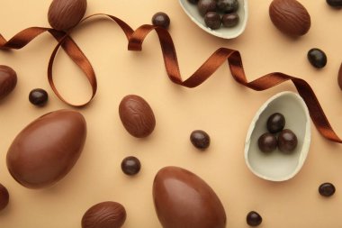 Paskalya kompozisyonu çikolatalı yumurta ve bej arka planda kahverengi kurdele. Üst görünüm