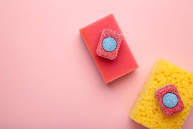 Bulaşık makinesi tabletleri pembe arka planda bulaşık süngeri, bulaşık ürünleri. Üst görünüm