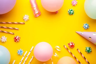Renkli karnaval ya da parti çerçeveli balonlar, flamalar ve sarı arka planda konfeti. Mesaj için yer var. Üst görünüm