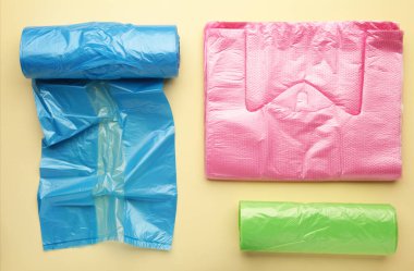 Bir sürü renkli plastik torba sarı arka planda yuvarlanıyor. Üst görünüm.