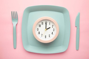 Top view of pink alarm clock with plate, fork and knife on pink background - concept and idea. Healthy food