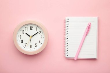 Pembe zemin üzerinde pembe alarm saati olan boş beyaz defter üst görünümü