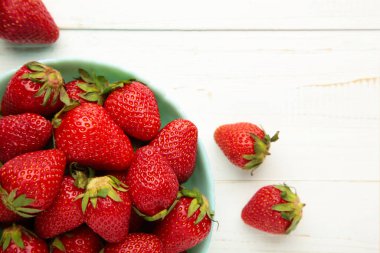 Beyaz arka planda mavi kasede olgun çilekler. Üst görünüm.