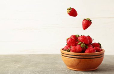 Çilekler gri arka planda ahşap kaseye düşer. Mesaj için yer var. Üst görünüm