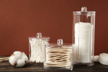 Cotton pads and cotton sticks in containers with cotton flower on brown background. Top view