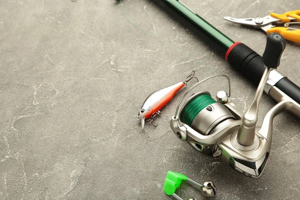 Fishing tackle - fishing spinning rod, hooks and lures on grey background. Active hobby recreation concept. Top view, flat lay.