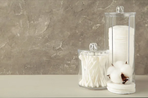 Cotton pads and cotton sticks in containers with cotton flower on grey background. Top view