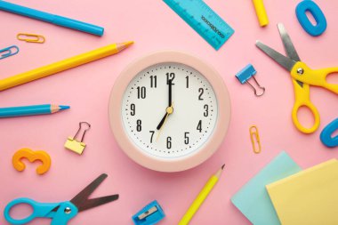 Çalar saat, boya, kalem ve makas. Pembe arka planda okul aksesuarları. Dikey fotoğraf.