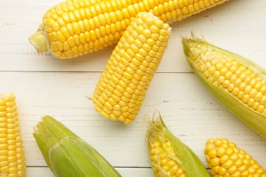 Fresh corn on cobs on white wooden background. Top view