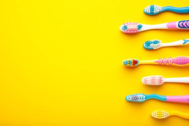 Colorful toothbrushes on yellow background with copy space. Top view