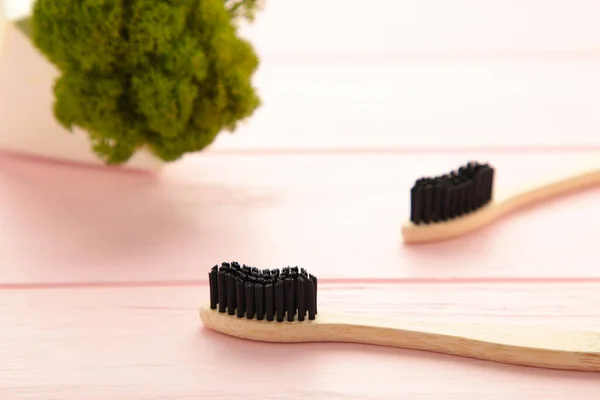 Bamboo wood toothbrush with black brush bristles on pink background. Top view