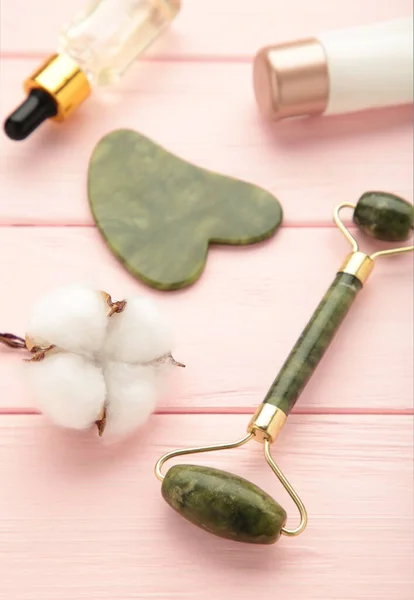 Green jade roller and gua sha stone for facial massage and on pink background. Home beauty and selfcare accessories. Face roller for anti age wrinkle treatment. Vertical photo