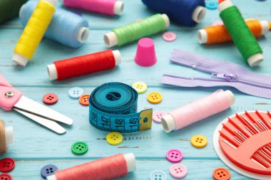 Mavi arka planda dikiş malzemeleri: dikiş ipliği, makas, büyük bir makara iplik, kumaş parçaları, iğneler, santimetre, düğmeler. Üst görünüm